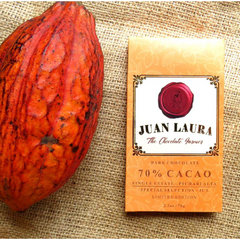 Verpackung der 70% dunklen Schokolade von Juan Laura mit rotem Siegel und orangefarbenem Muster, liegend auf Jutestoff neben einer großen orangefarbenen Kakaofrucht. Text: '70% CACAO', 'Single Estate - Pichari Alta', 'Special Selection - JL-2', 'Limited Edition', '2.5 oz / 70 g'.
