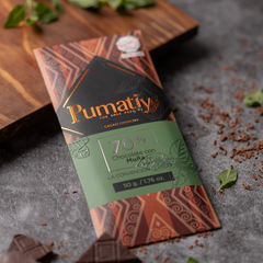 Pumatiy Schokolade mit 70% Kakaoanteil und Muña, kunstvoll inszeniert auf einem dunklen Hintergrund mit frischen Minzblättern und Kakaosplittern. Die Tafel ist elegant verpackt mit einem Design, das traditionelle peruanische Muster und natürliche Elemente vereint.