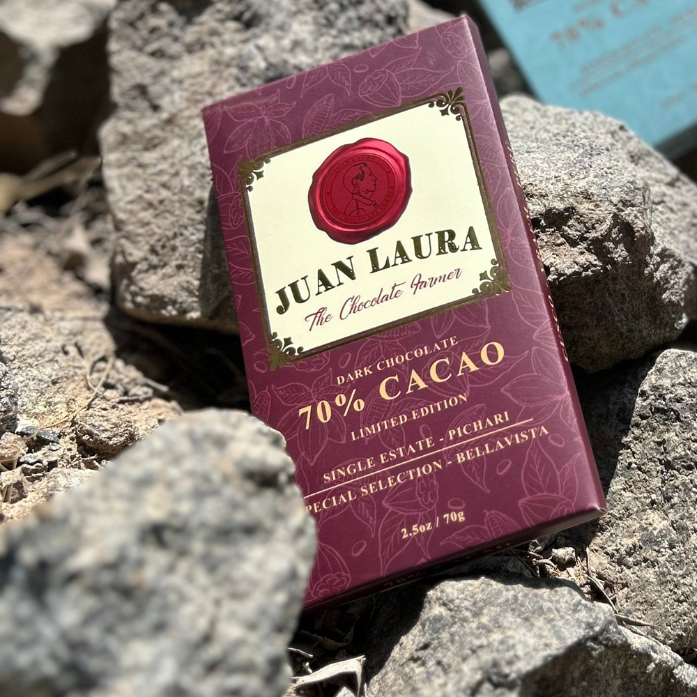 Juan Laura 70% Kakao Schokolade auf einem natürlichen, felsigen Hintergrund. Die burgunderrote Verpackung hebt sich kontrastreich von den Steinen ab und betont die Ursprünglichkeit und den natürlichen Ursprung des Kakaos.