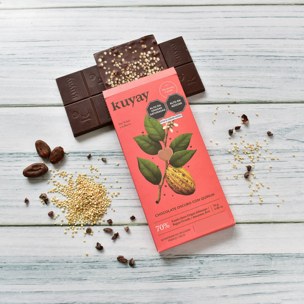 Kuyay Schokolade mit Quinoa, 70% Kakao, auf einem hellen Holzuntergrund. Die Schokoladentafel ist geöffnet und zeigt Quinoa-Stückchen in der Schokolade, umgeben von rohen Kakaobohnen, Quinoa und Kakaonibs als Dekoration.