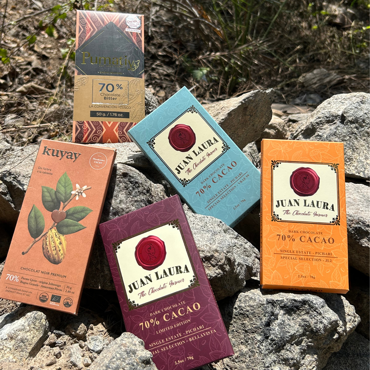 “Fünf Tafeln 70%-Schokolade aus dem Tasting-Paket von Chukulati, arrangiert auf natürlichen Steinen in der Natur. Schokoladen von Juan Laura, Kuyay und Pumatiy, jede mit einzigartigem Design und handwerklicher Qualität.”