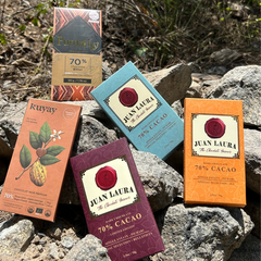 “Fünf Tafeln 70%-Schokolade aus dem Tasting-Paket von Chukulati, arrangiert auf natürlichen Steinen in der Natur. Schokoladen von Juan Laura, Kuyay und Pumatiy, jede mit einzigartigem Design und handwerklicher Qualität.”